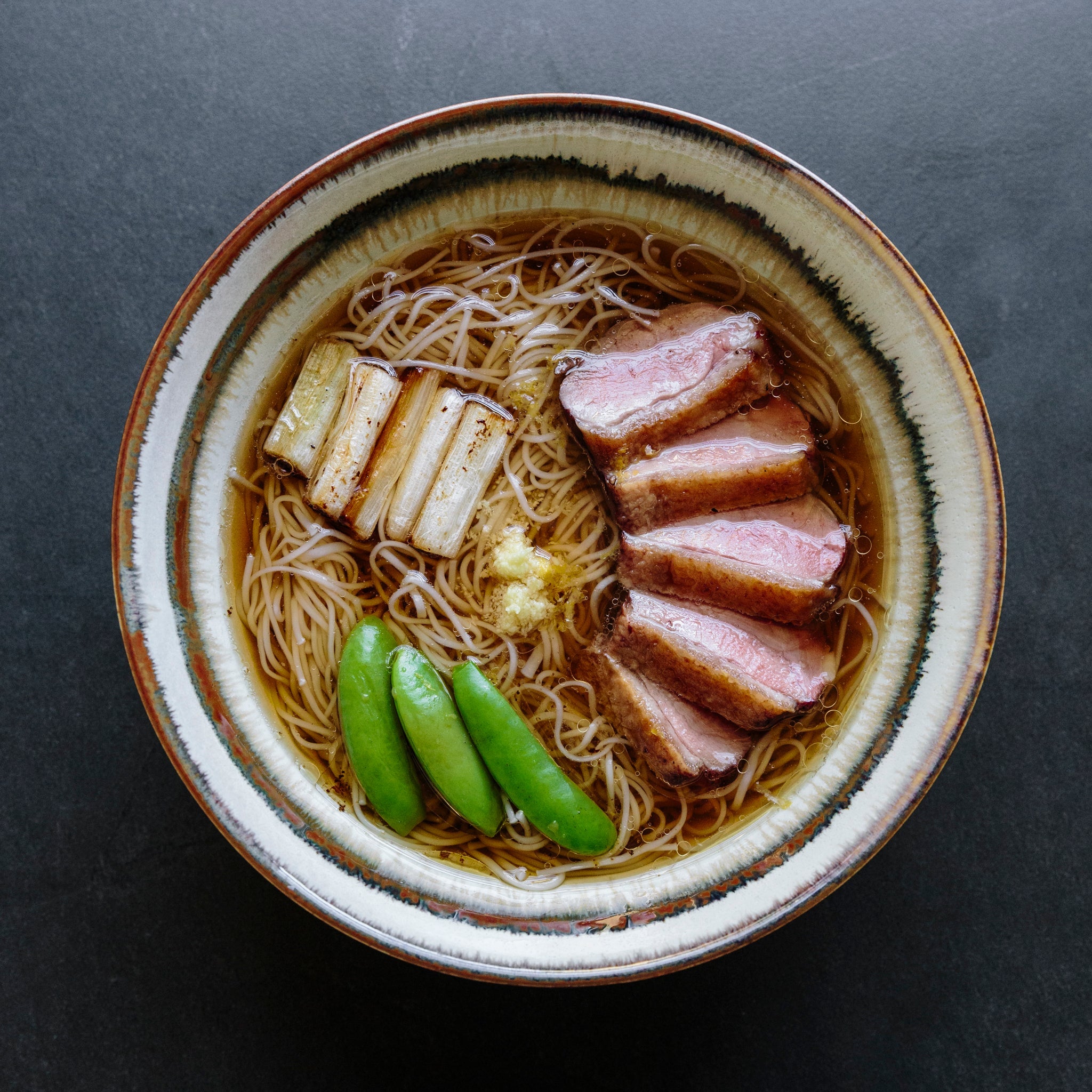 A bowl of somen noodles with duck and snap peas in a savory broth