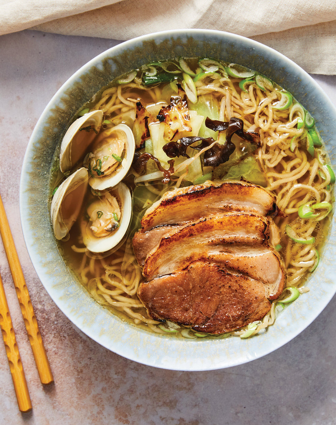 Bowl of ramen with clams, pork, and vegetables on a light background