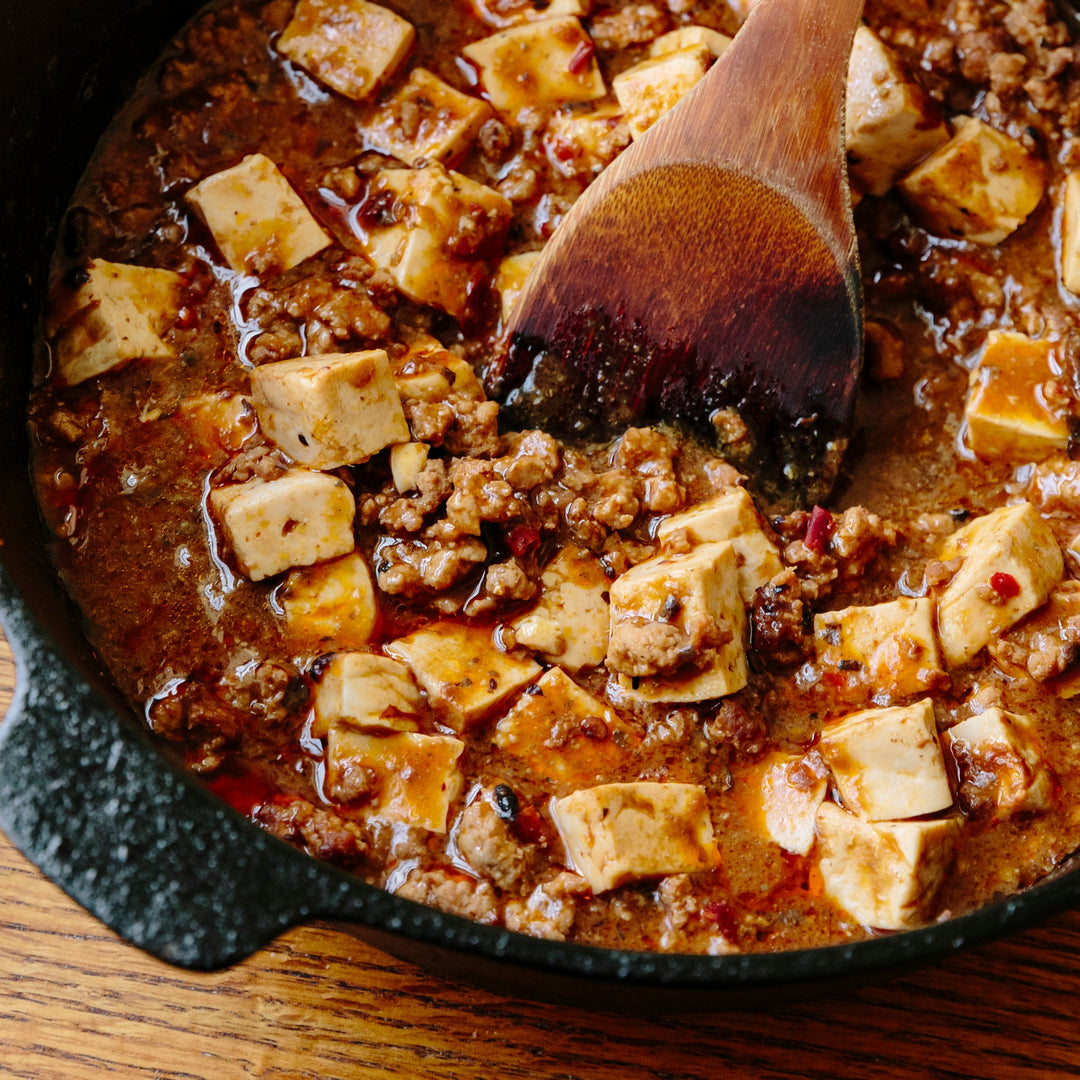 A pan of Mapo Tofu being stirred by a wooden spoon