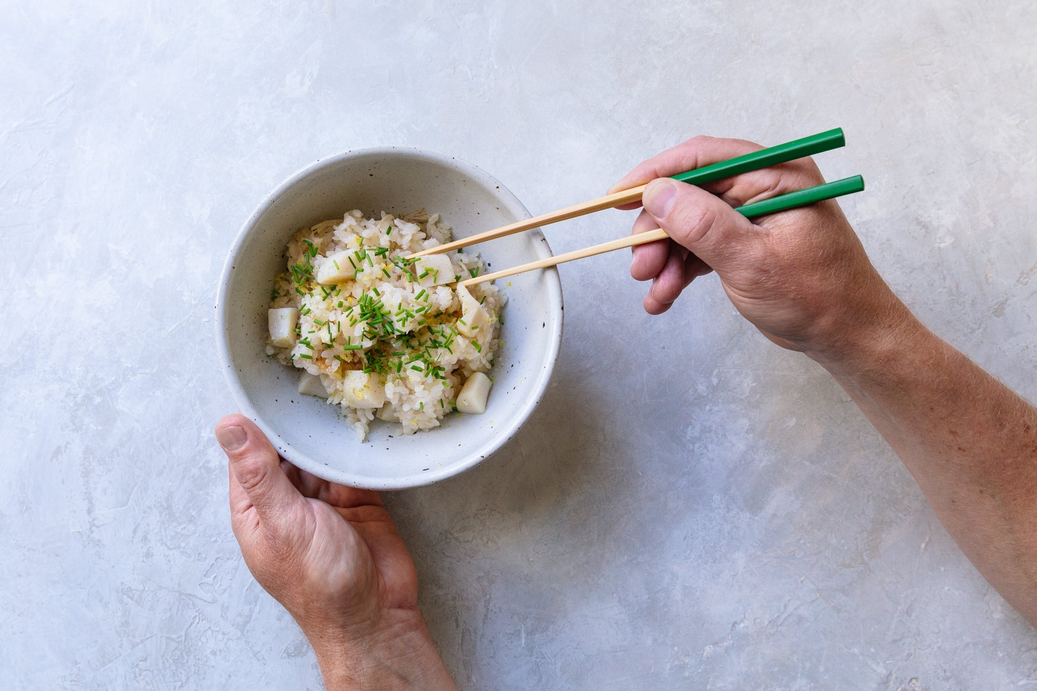 Person holding a bowl of food with chopsticks on a light background