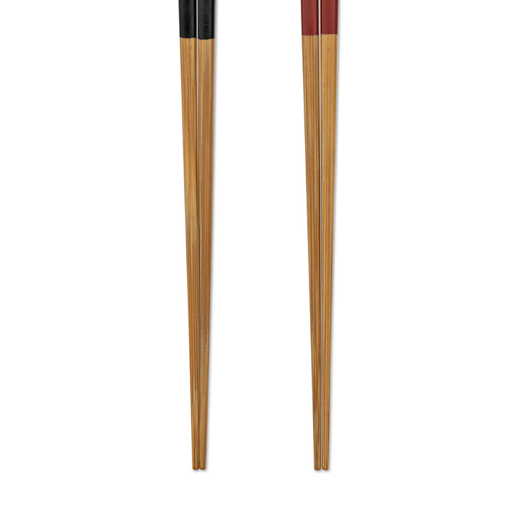 Closeup of a pair of wooden chopsticks with black and red handles and brown wooden tips on a white background