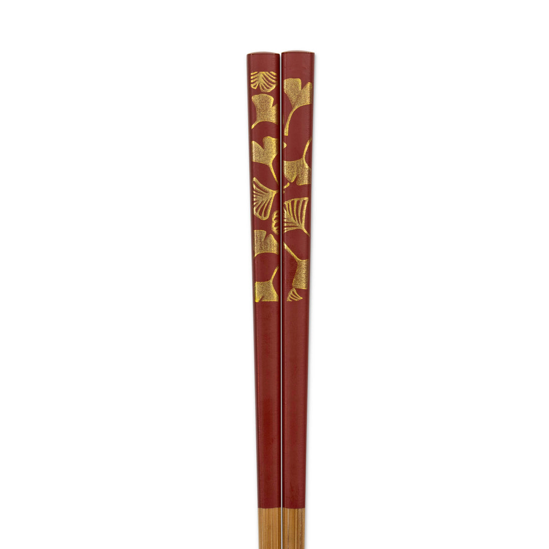 Red chopsticks with gold leaf gingko patterns on a white background
