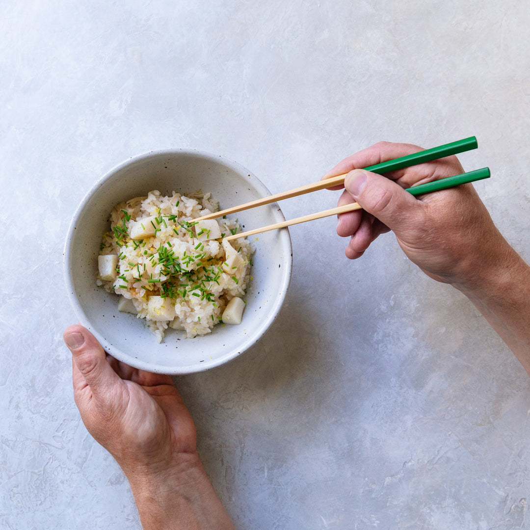 Person holding a bowl of food with chopsticks on a light background