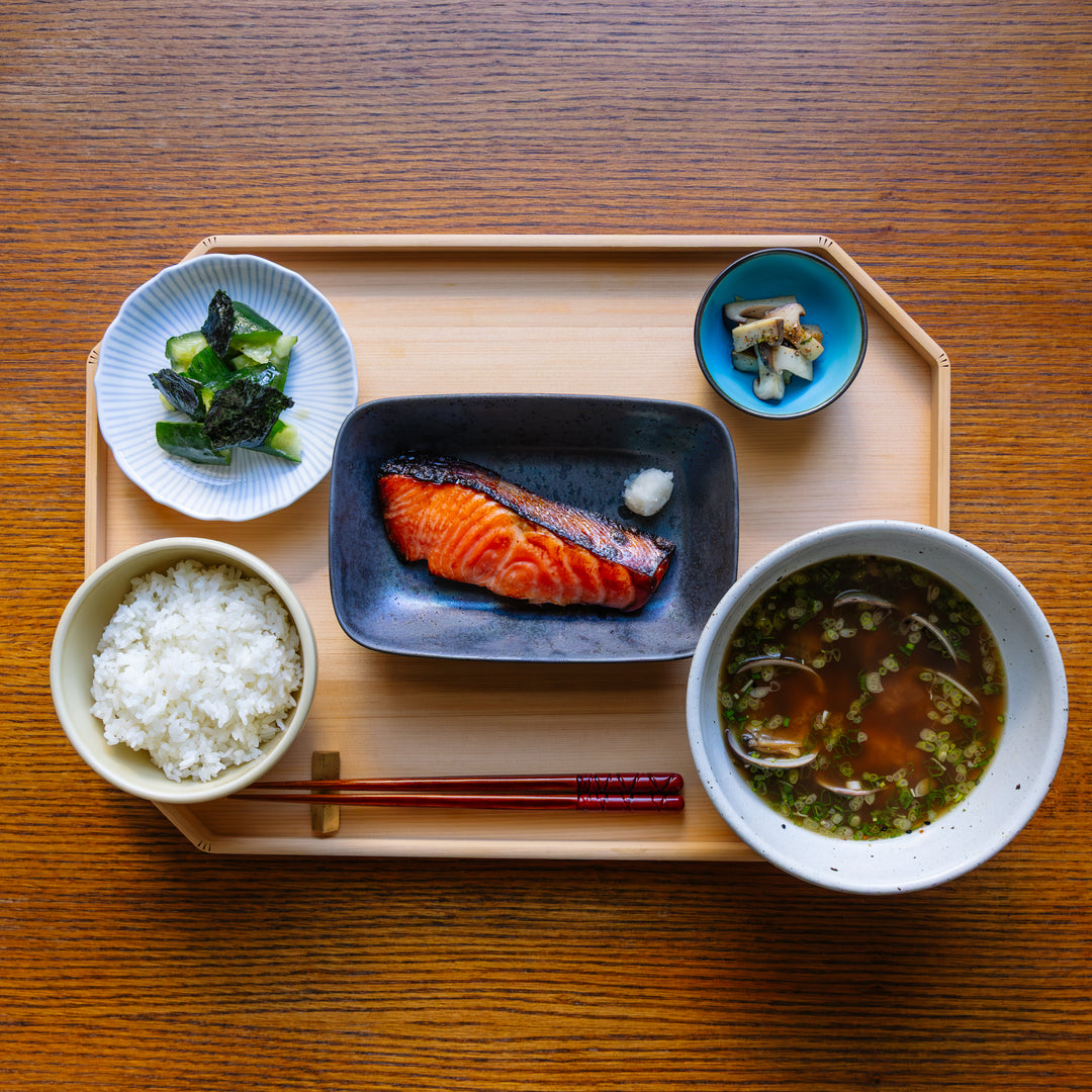 Japanese meal set on a wooden tray with salmon, rice, soup, and vegetables.