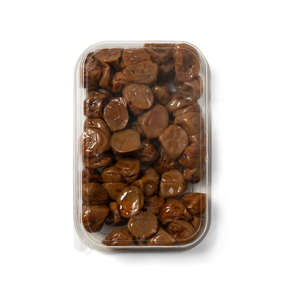 A clear plastic clamshell container filled with pickled Japanese plums, photographed from above on a white background.