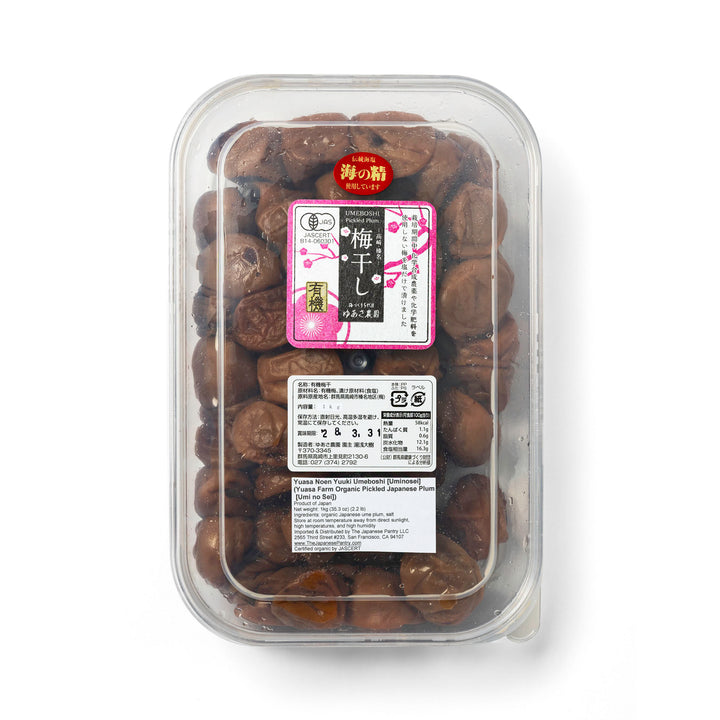 A clear plastic clamshell package containing dark brown pickled Japanese plums, with a Japanese label on the front, isolated on a white background.