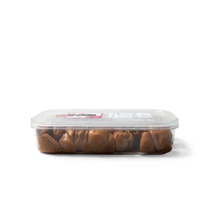 A clear plastic tub of pickled Japanese plums with a transparent lid and a small product label, photographed on a plain white background.