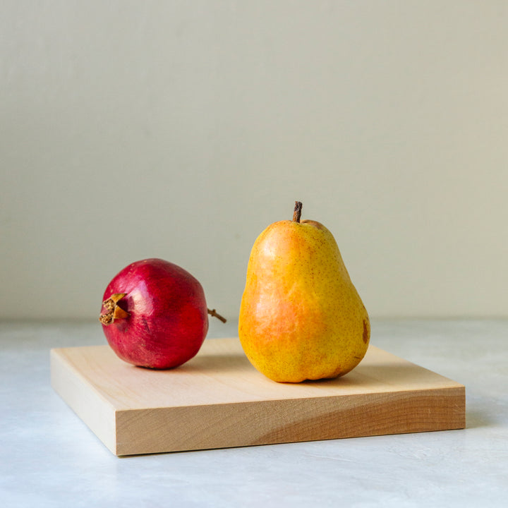Side shot of a medium cutting board with a yellow pear and a red persimmon on it.