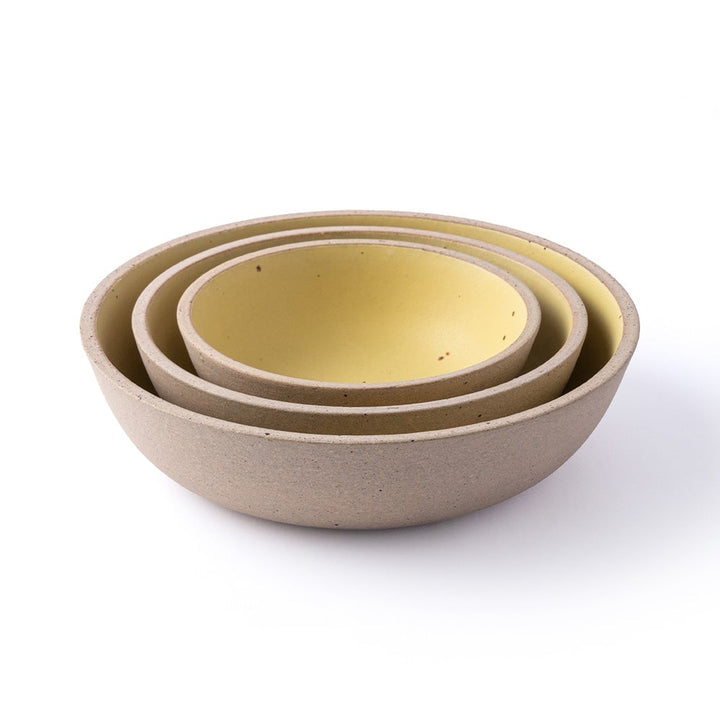 Three nested ceramic bowls with a speckled beige exterior and a matte yellow interior, photographed on a clean white background.