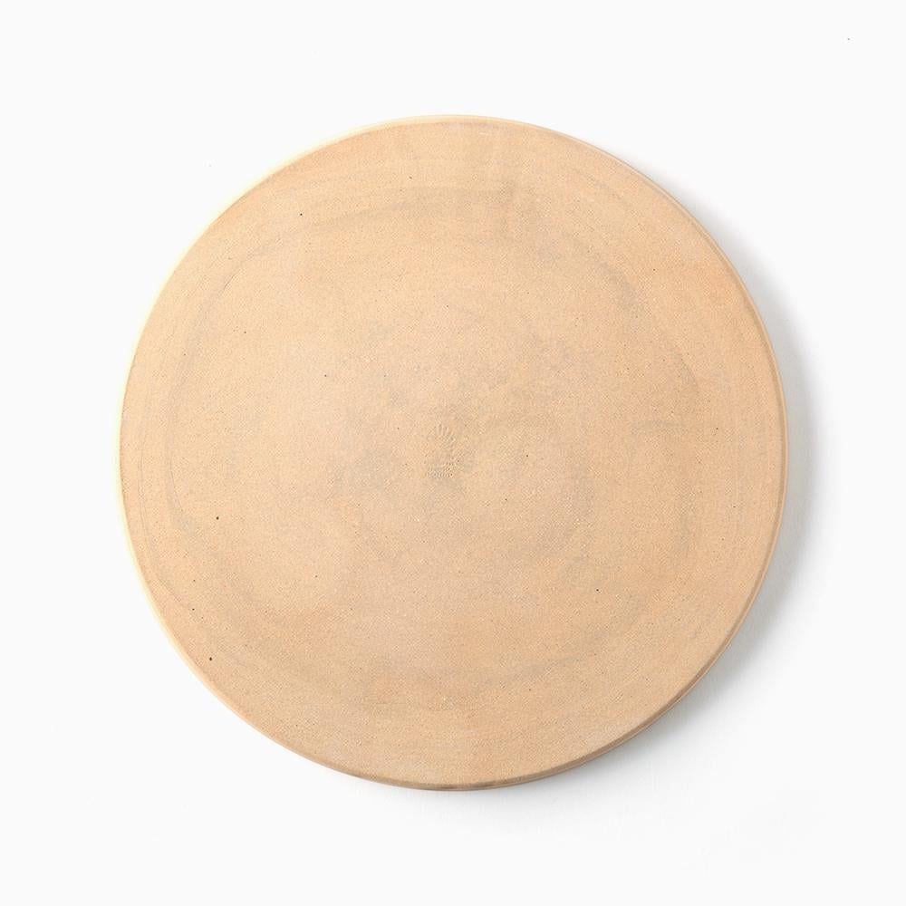 Bottom of a round, light beige ceramic plate or shallow dish with a matte, slightly textured finish.