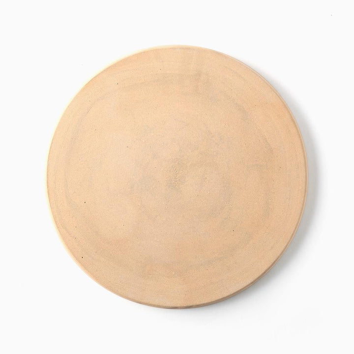 Bottom of a round, light beige ceramic plate or shallow dish with a matte, slightly textured finish.