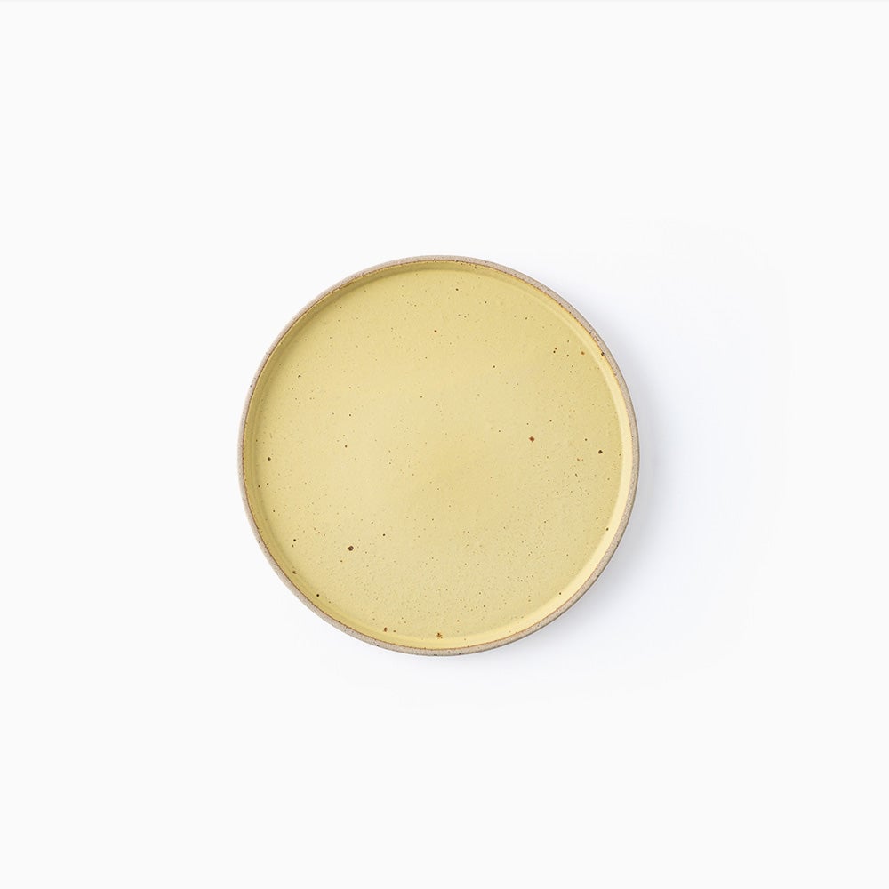 A round ceramic plate with a speckled light yellow glaze and a natural beige rim, photographed from directly above on a clean white background.