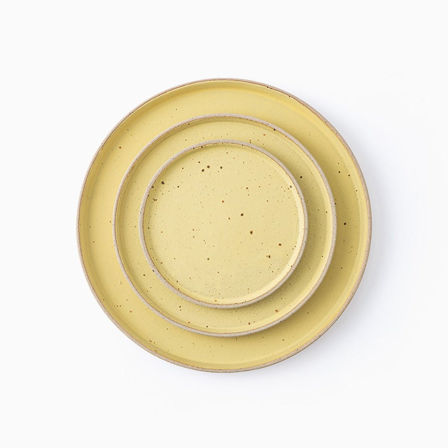 Three nested ceramic plates in a light yellow speckled glaze, photographed from directly above on a clean white background.