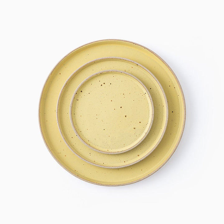 Three nested ceramic plates in a light yellow speckled glaze, photographed from directly above on a clean white background.