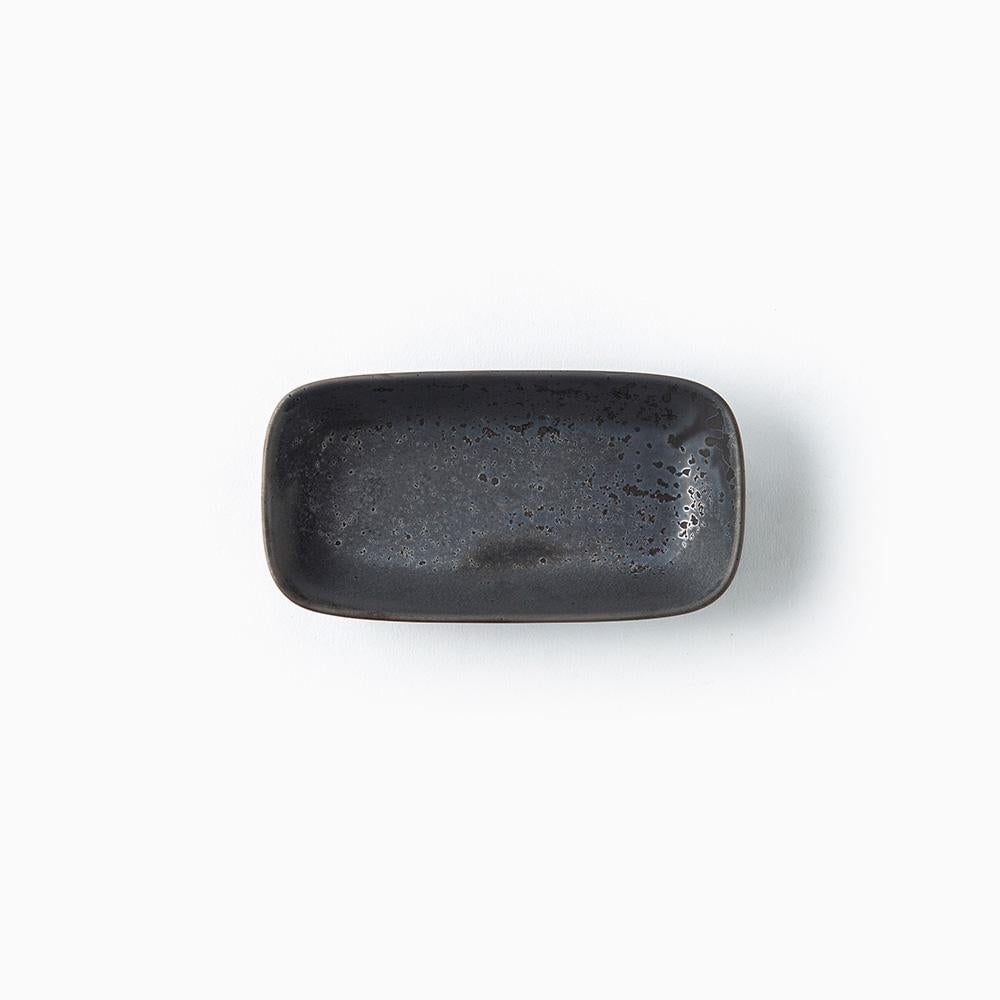 A small rectangular ceramic dish with rounded corners, featuring a dark charcoal gray to black speckled glaze, shown from a top-down view on a white background.